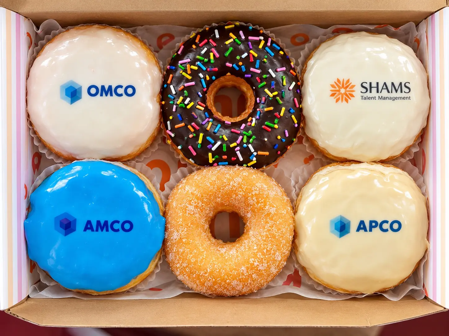 A close-up box of donuts individually customized with company logos